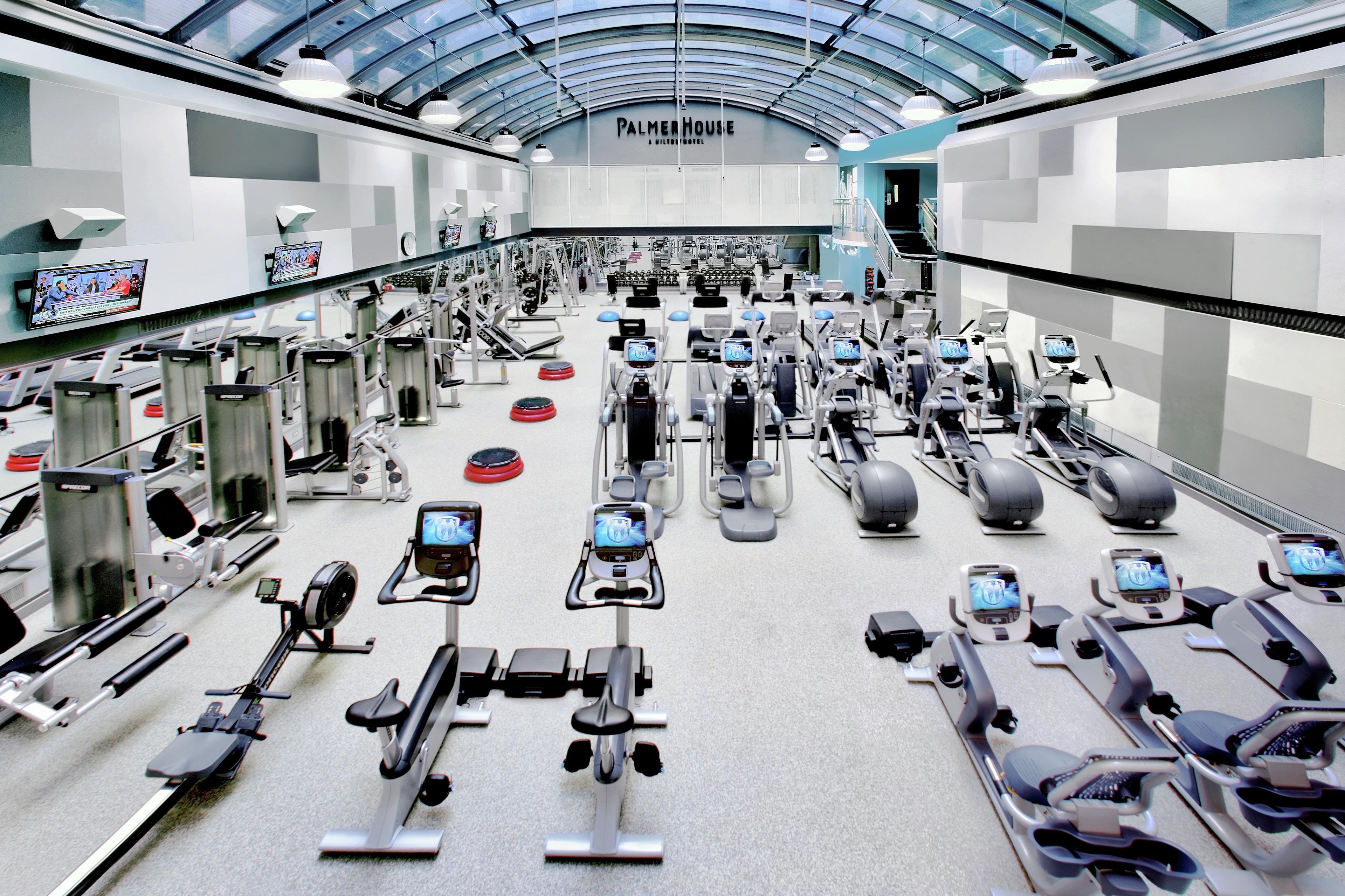 A gym with various exercise equipment, a large mirror, and a ceiling with a glass structure.