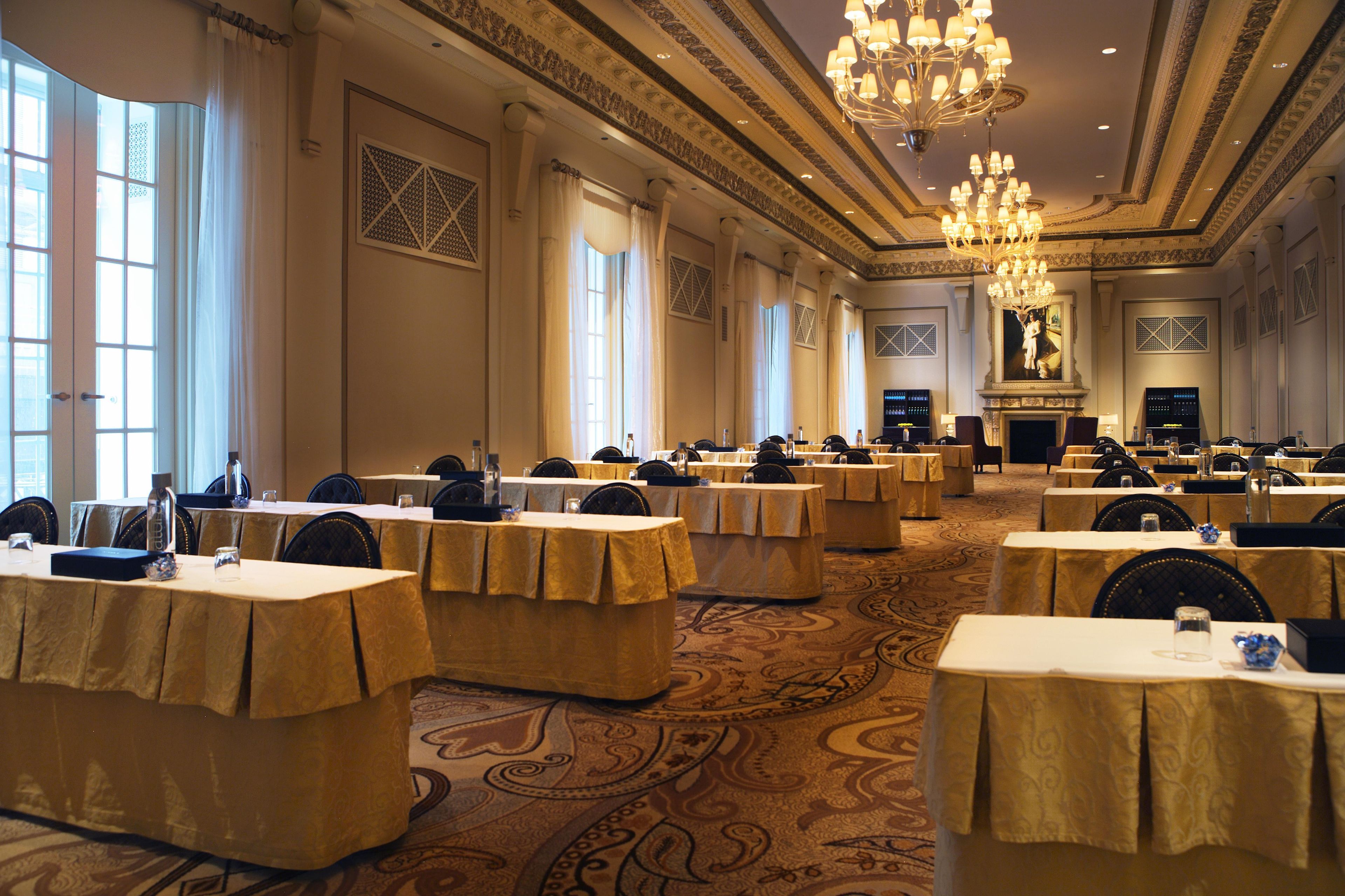 A banquet hall with multiple round tables, each covered with a tablecloth, and a large chandelier hanging from the ceiling.