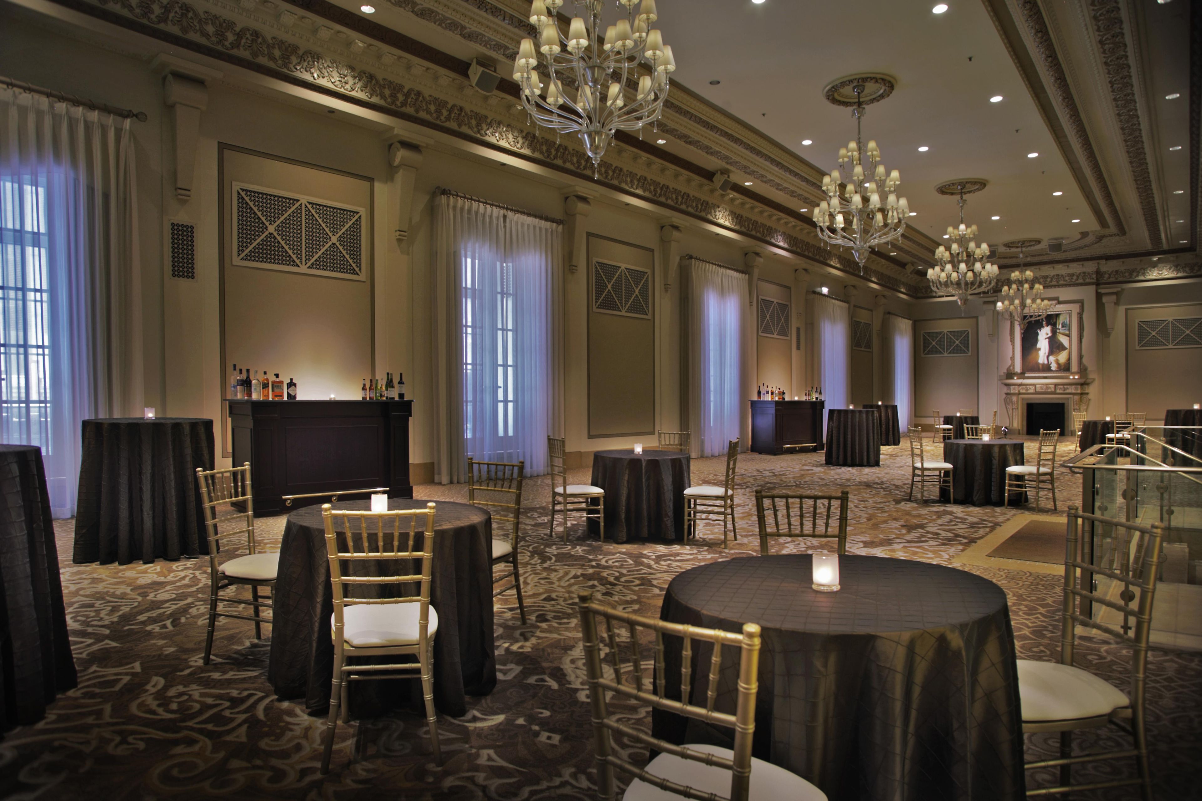 Une salle de banquet spacieuse, dotée de tables rondes, de chaises, de lustres et d’une cheminée.