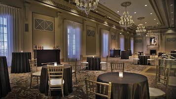 Une salle de banquet spacieuse, dotée de tables rondes, de chaises, de lustres et d’une cheminée.