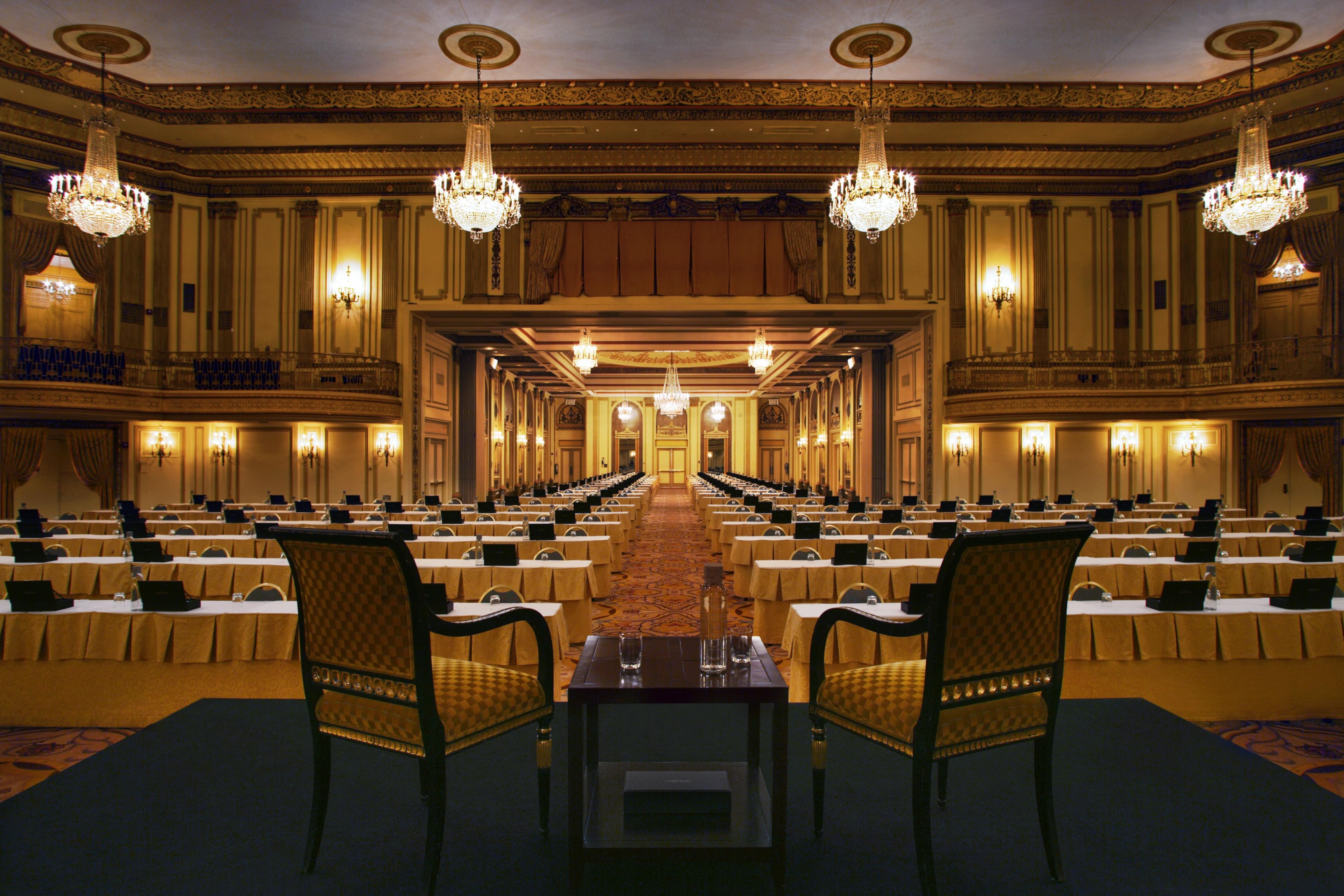 A banquet hall with rows of tables, chandeliers, and ornate wall decorations.