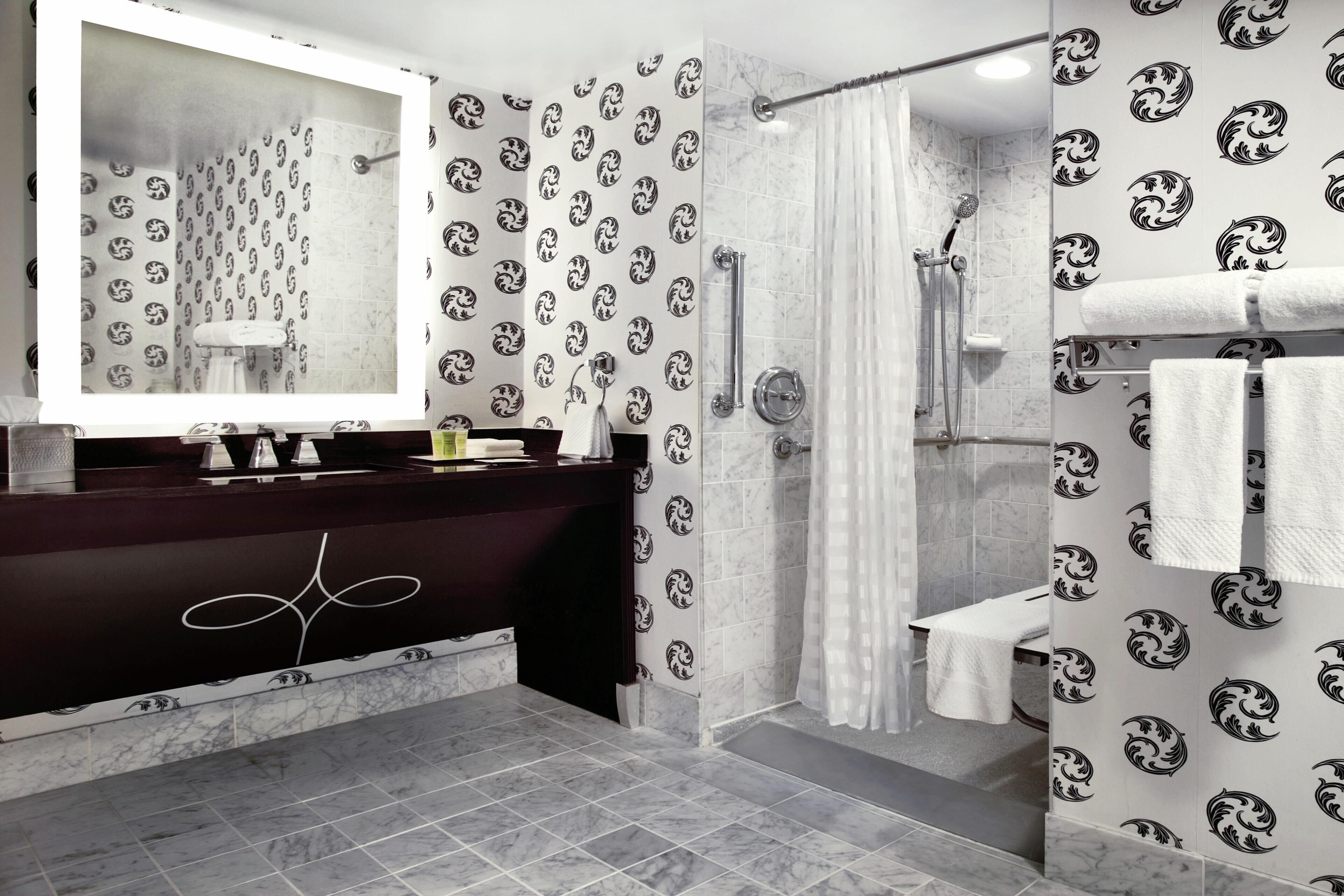 A modern bathroom with a dark vanity, a large mirror, a shower with a glass door, and patterned wallpaper.