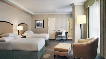 A hotel room with two beds, a desk, a chair, and a lamp.