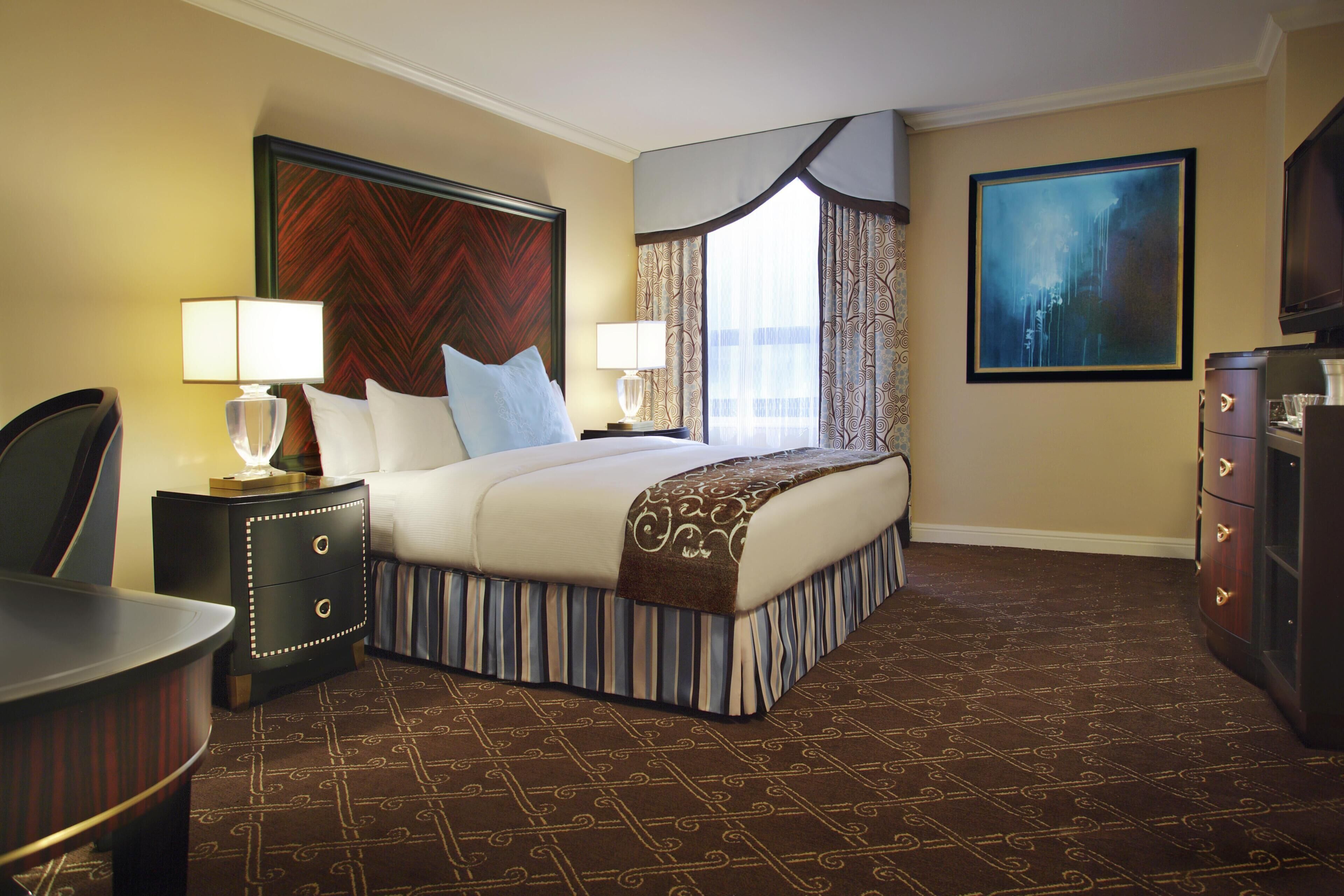 A hotel room with a bed, two bedside tables, a chair, a dresser, and a painting on the wall.
