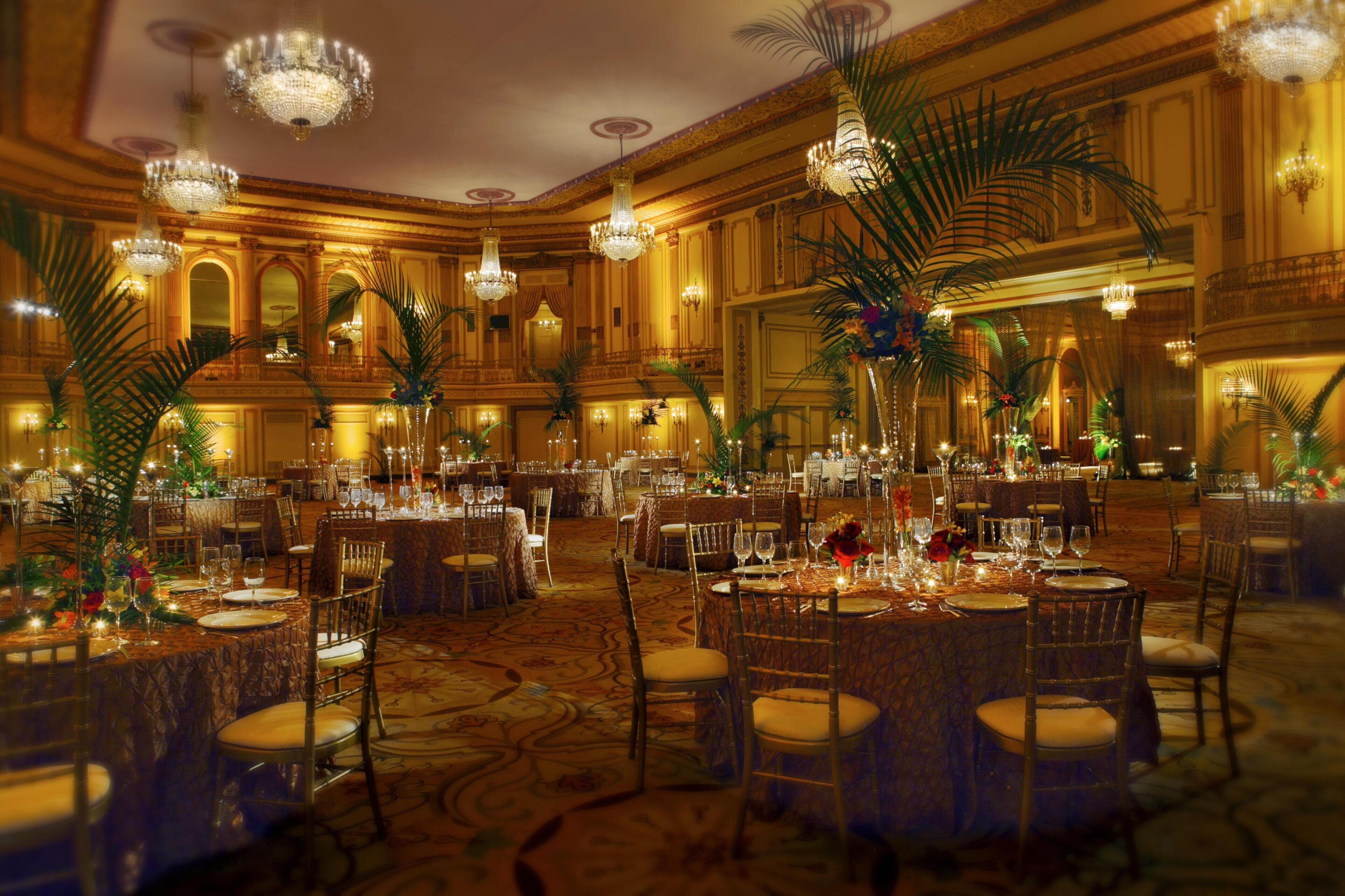 A banquet hall with round tables, chandeliers, and ornate wall decorations.