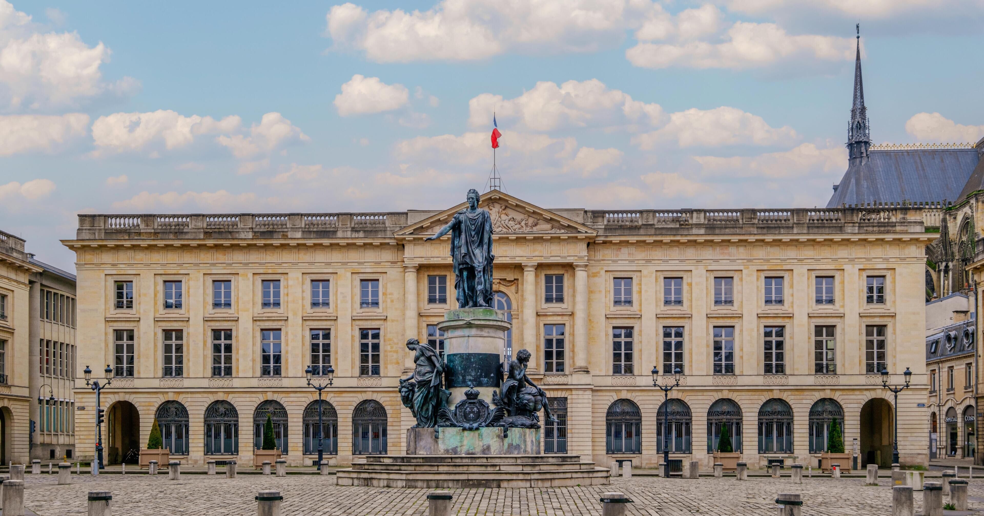 Un edificio histórico con una estatua central, ventanas arqueadas y una plaza adoquinada.