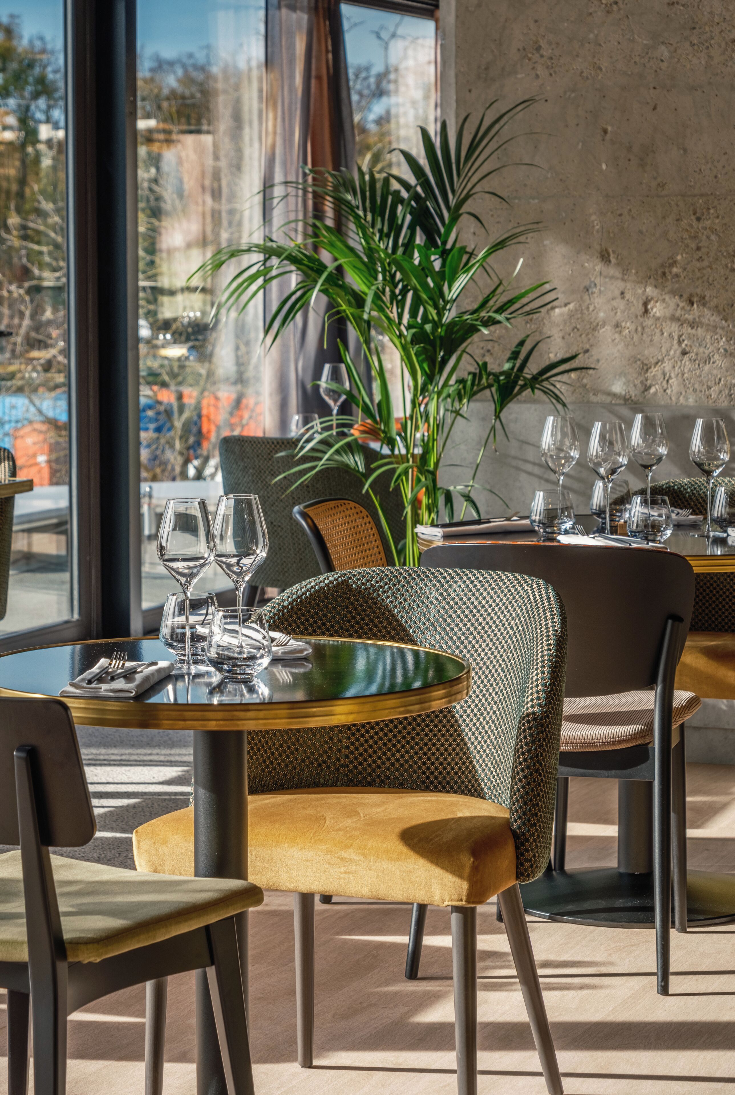 A restaurant interior with a dining table set for two, a potted plant, and a view through large windows.