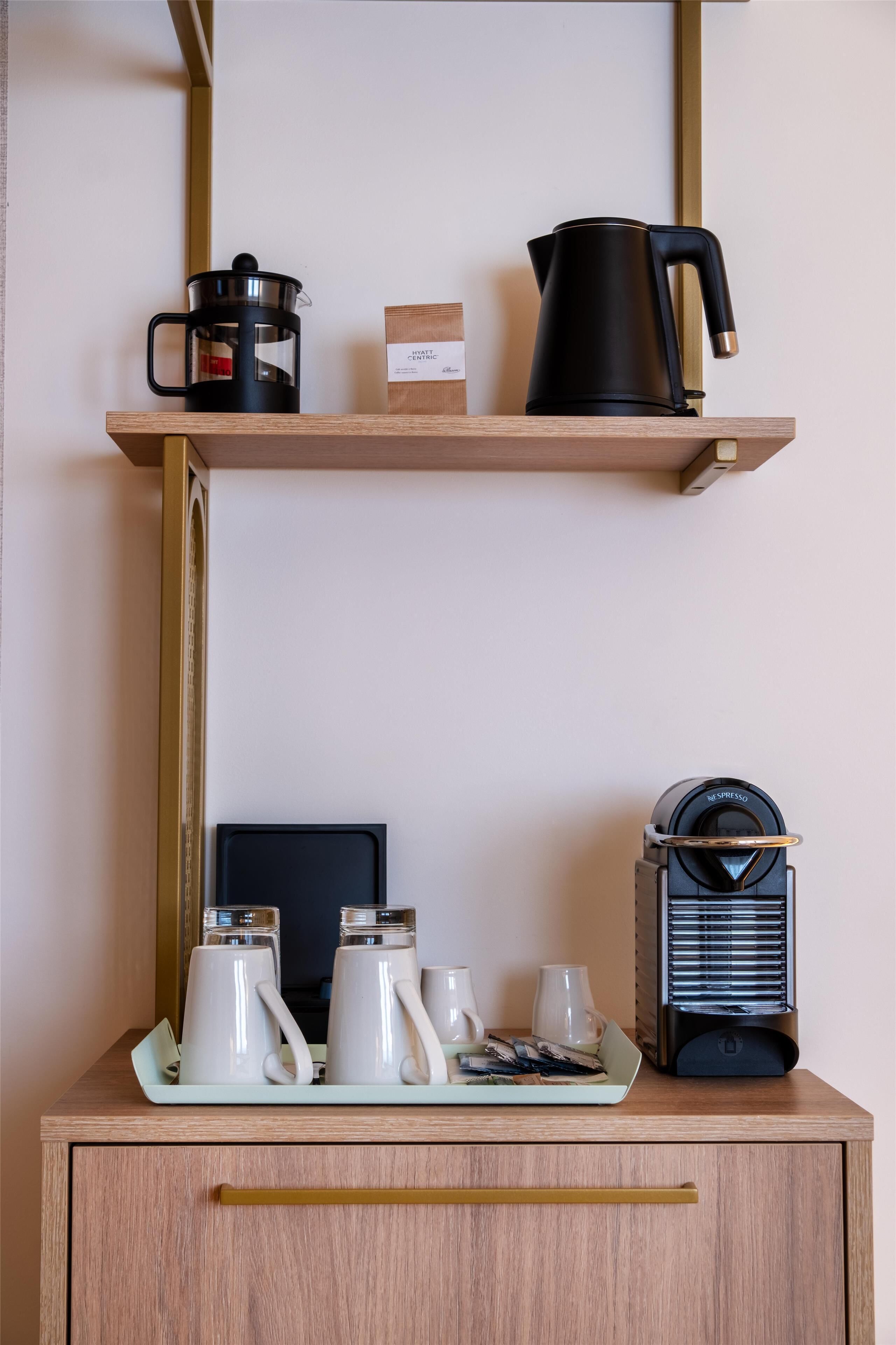 Una kitchenette con cafetera, hervidor de agua y un plato de comida sobre una encimera de madera.