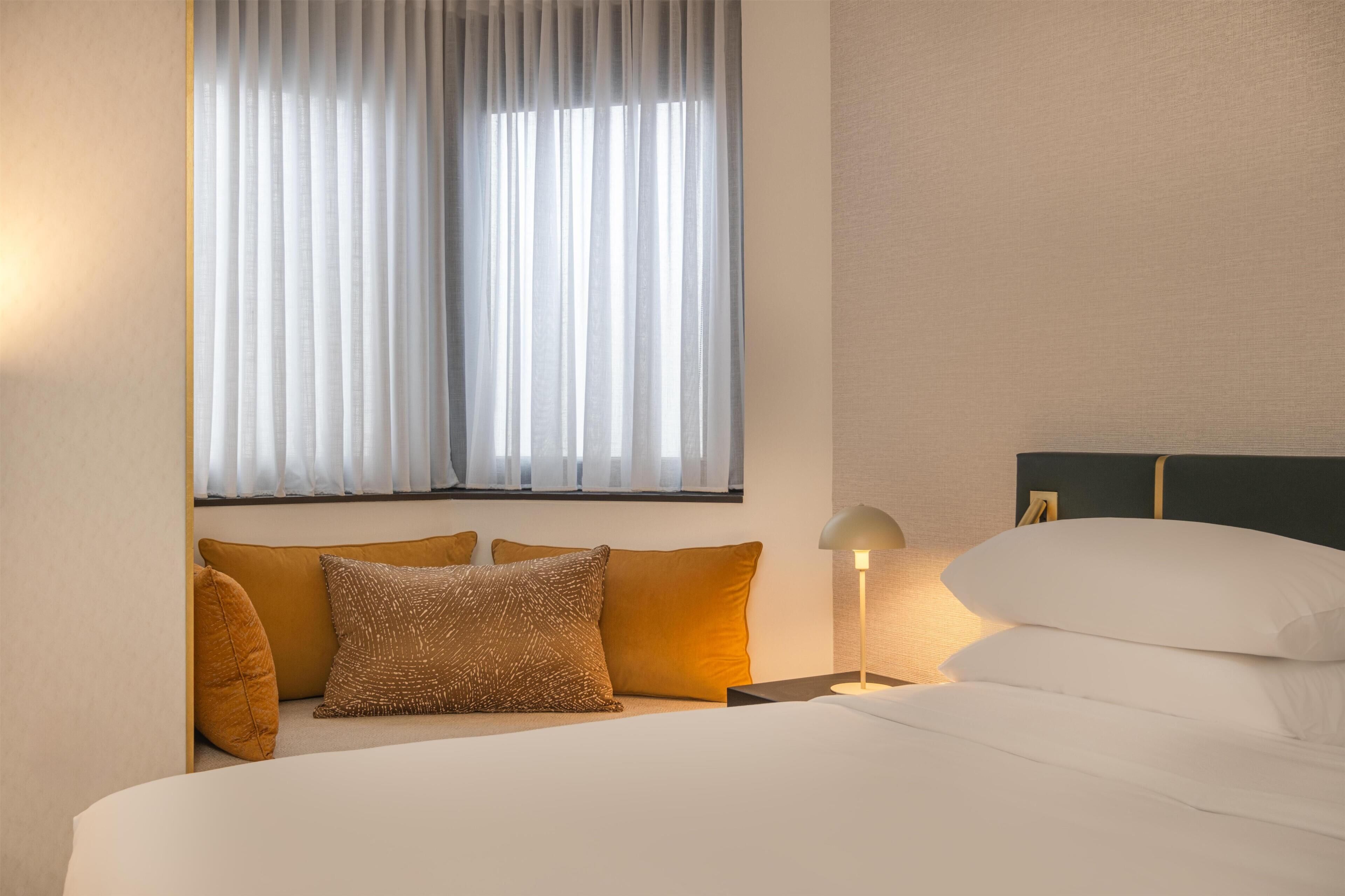 Un lit bien fait, avec des draps blancs, une tête de lit et une lampe de chevet.