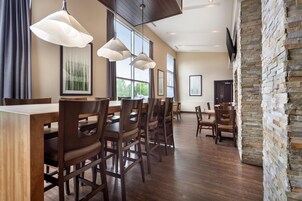 Comedor con mesas y sillas de madera, iluminación colgante, ventanas amplias y una pared decorativa de piedra.
