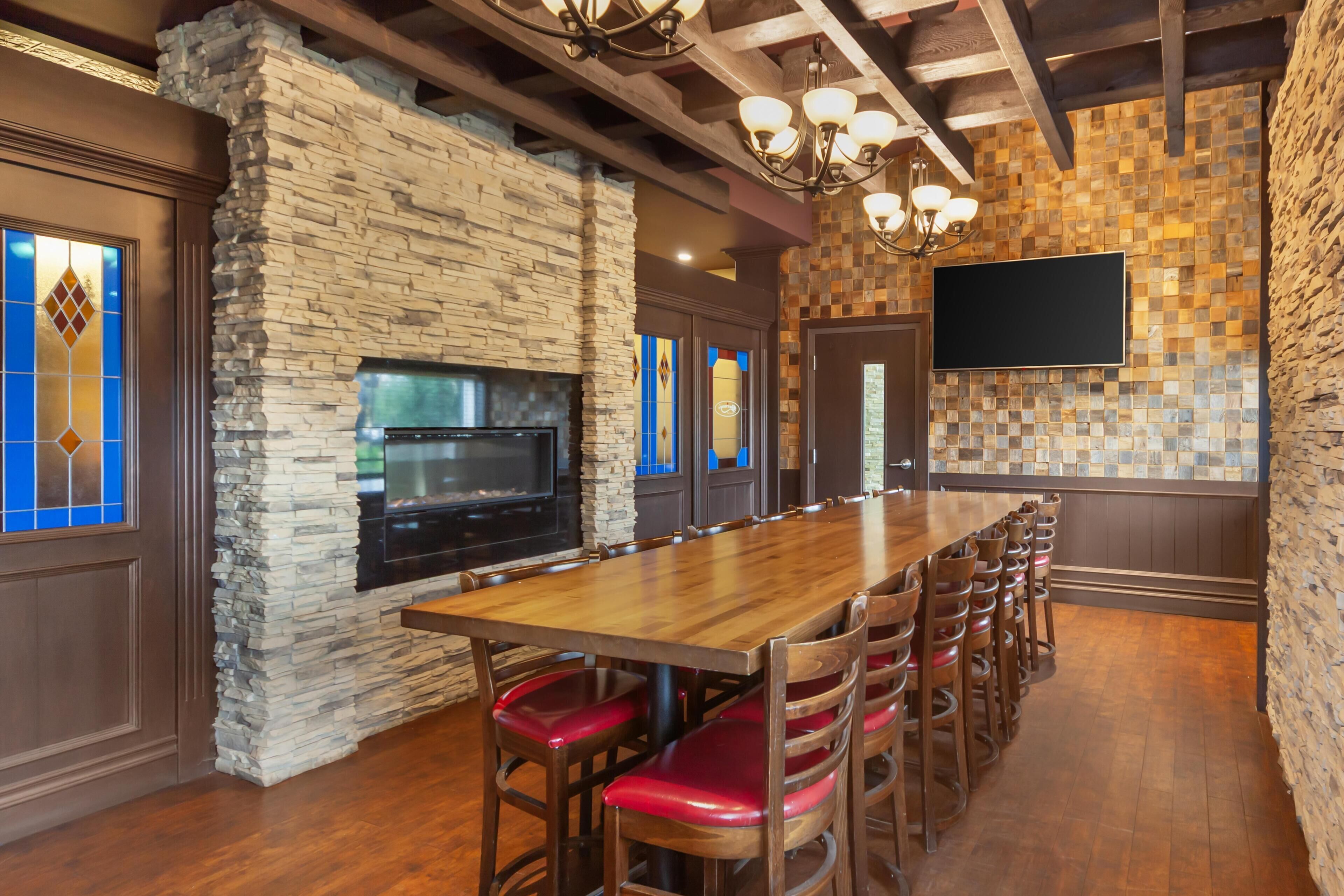 Una larga mesa de madera con sillas con cojines rojos, una chimenea de piedra y una pared de azulejos.