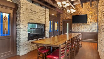 Una larga mesa de madera con sillas con cojines rojos, una chimenea de piedra y una pared de azulejos.