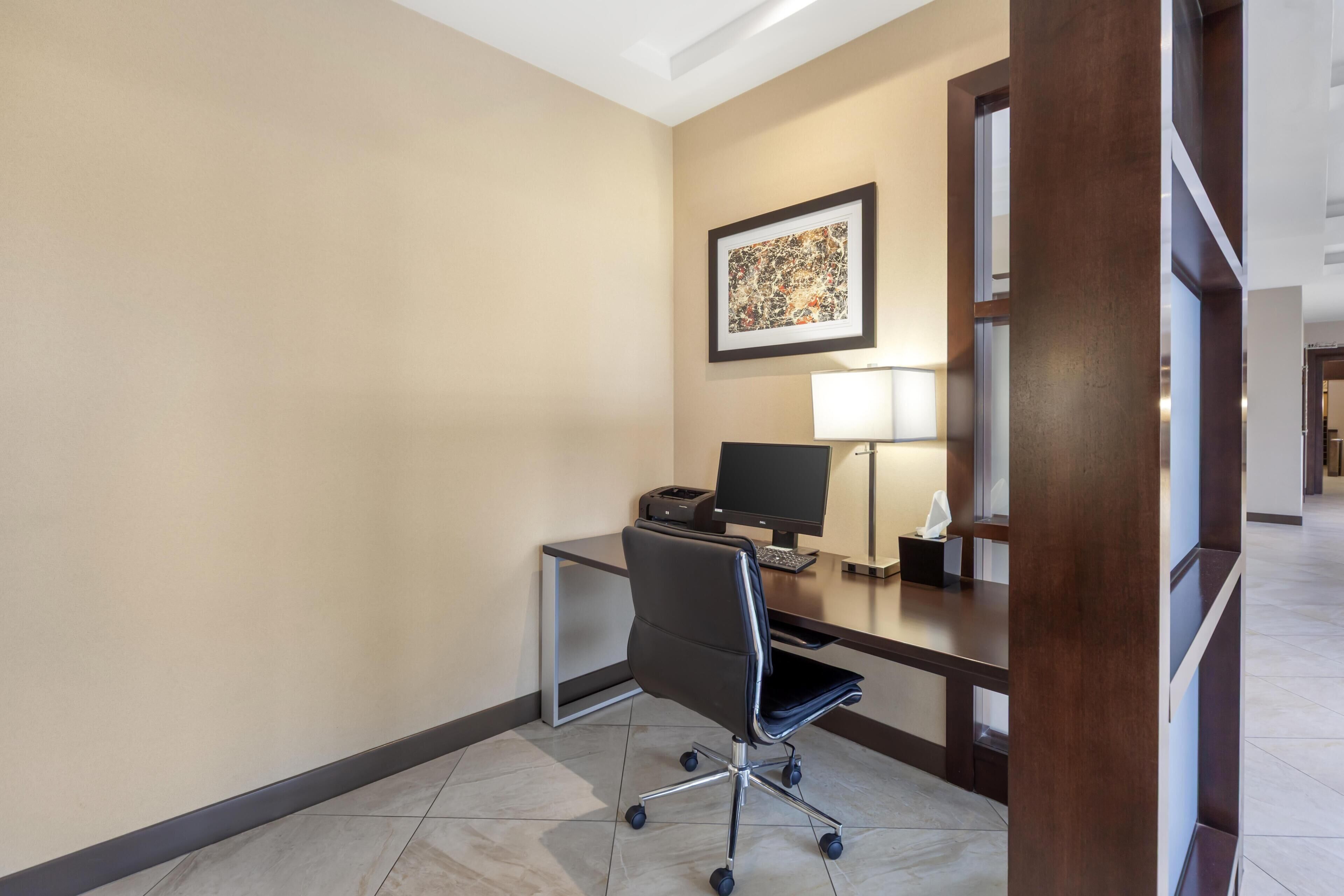 A hotel room with a desk, chair, lamp, and a framed artwork on the wall.