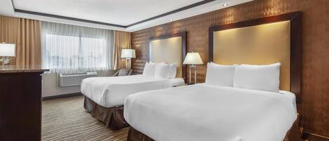 A hotel room with two beds, a desk, a window with curtains, and a patterned carpet.