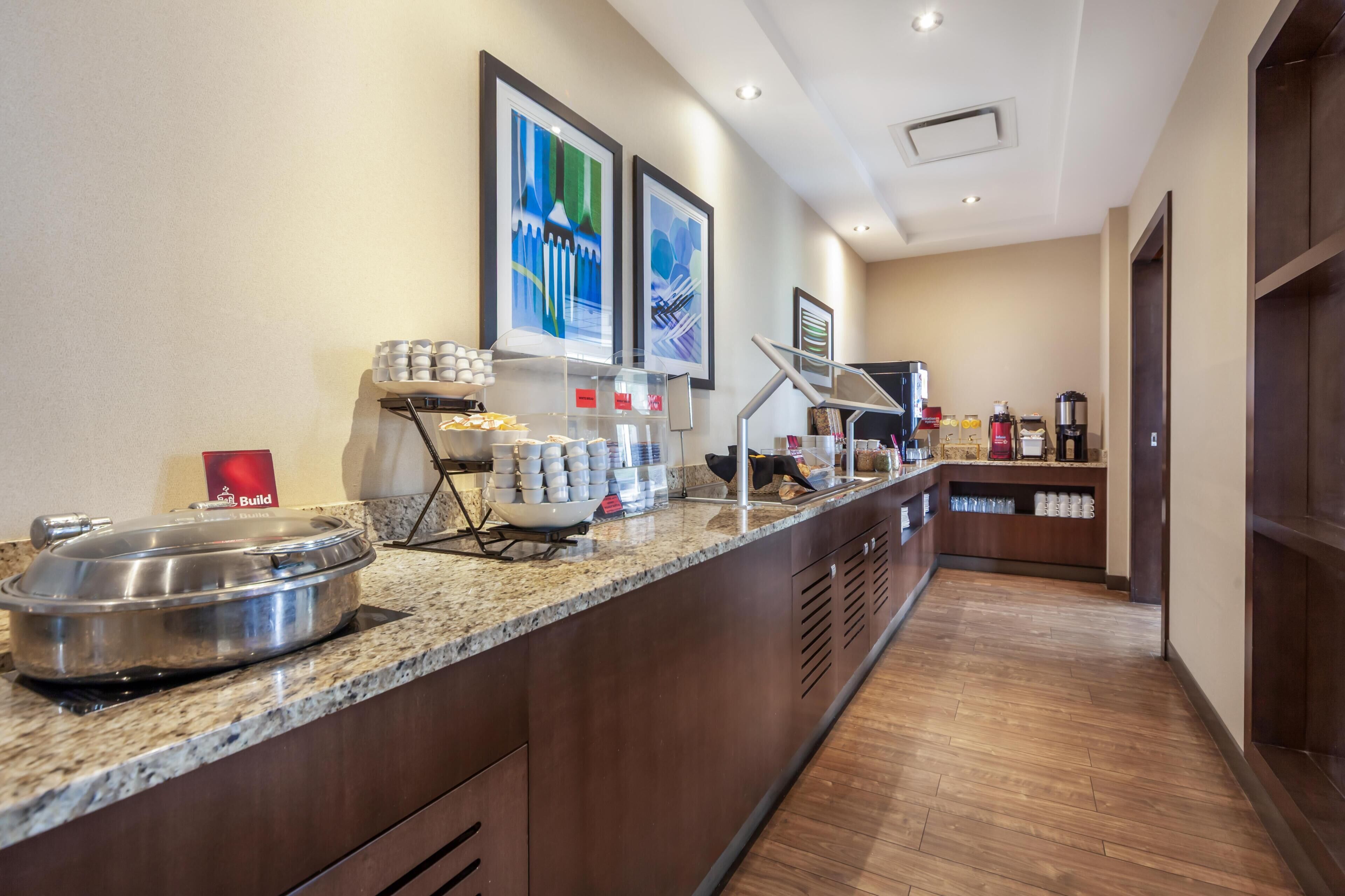 A hotel breakfast area with a granite countertop, coffee station, and framed artwork on the wall.