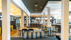 Un interior moderno con una barra central, diferentes disposiciones de asientos y una cocina visible al fondo.