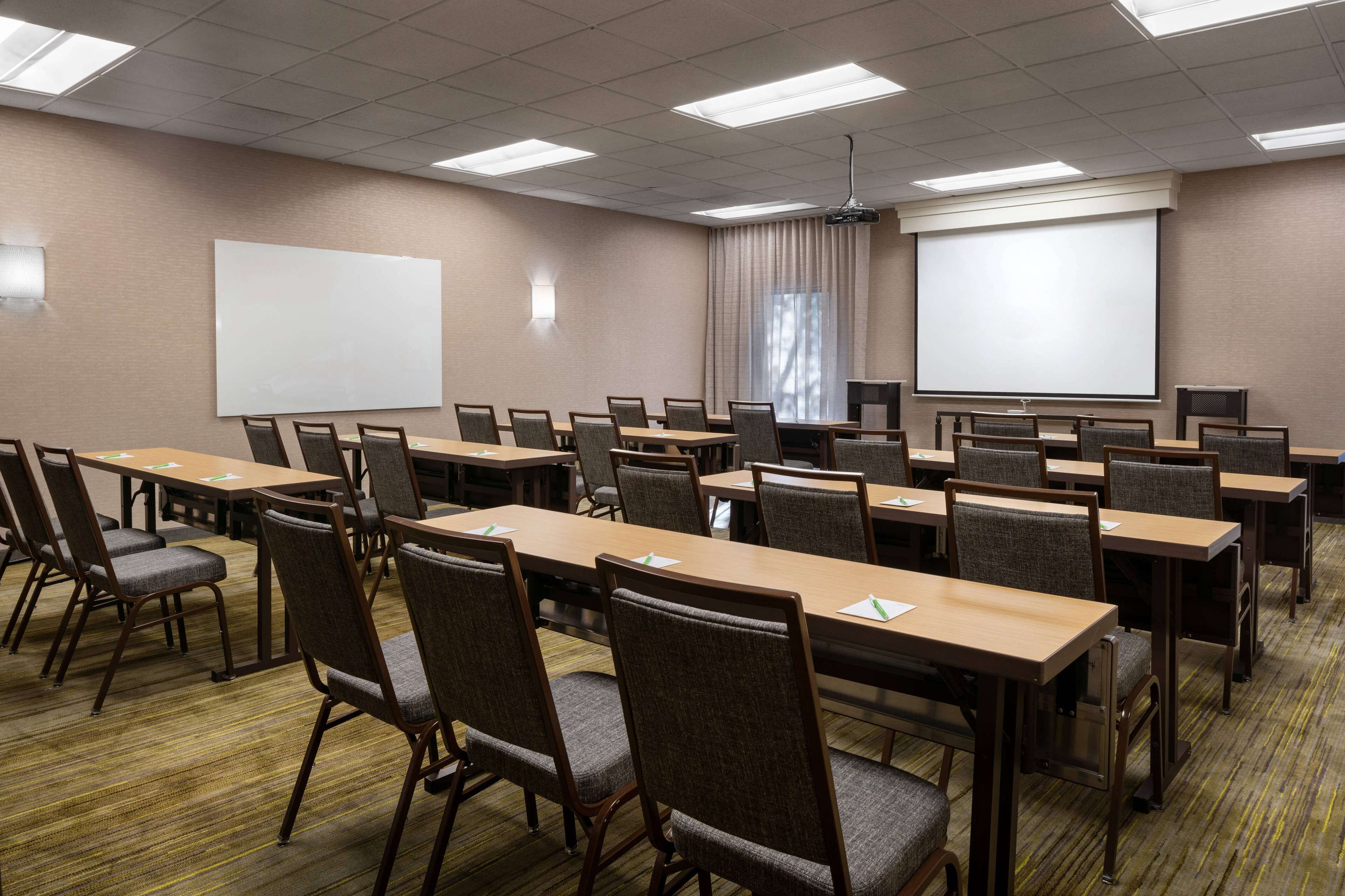 Un salón de conferencias con varias mesas y sillas, una pizarra y una pantalla de proyector.