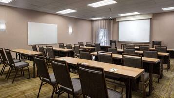 Un salón de conferencias con varias mesas y sillas, una pizarra y una pantalla de proyector.