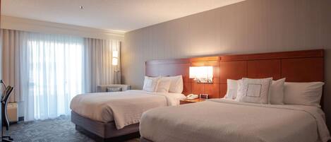 A hotel room with two beds, a desk, a chair, and a large window with curtains.