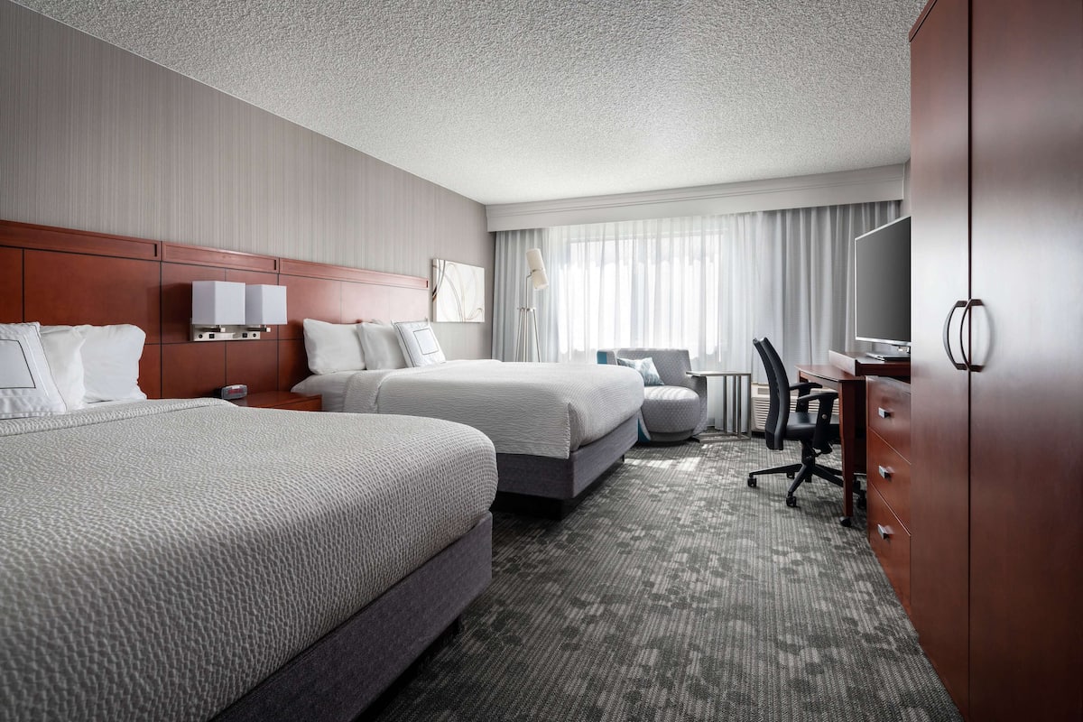 A hotel room with two beds, a desk, a chair, a TV, and a wardrobe.