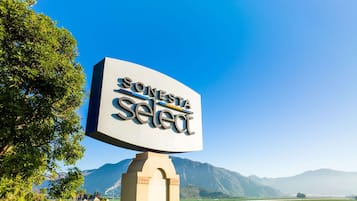 Un gran letrero con el texto "SONESTA Select" contra un cielo azul claro, con montañas al fondo.