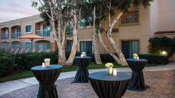 Un patio con cuatro mesas redondas, cada una con un mantel oscuro y un jarrón de flores.