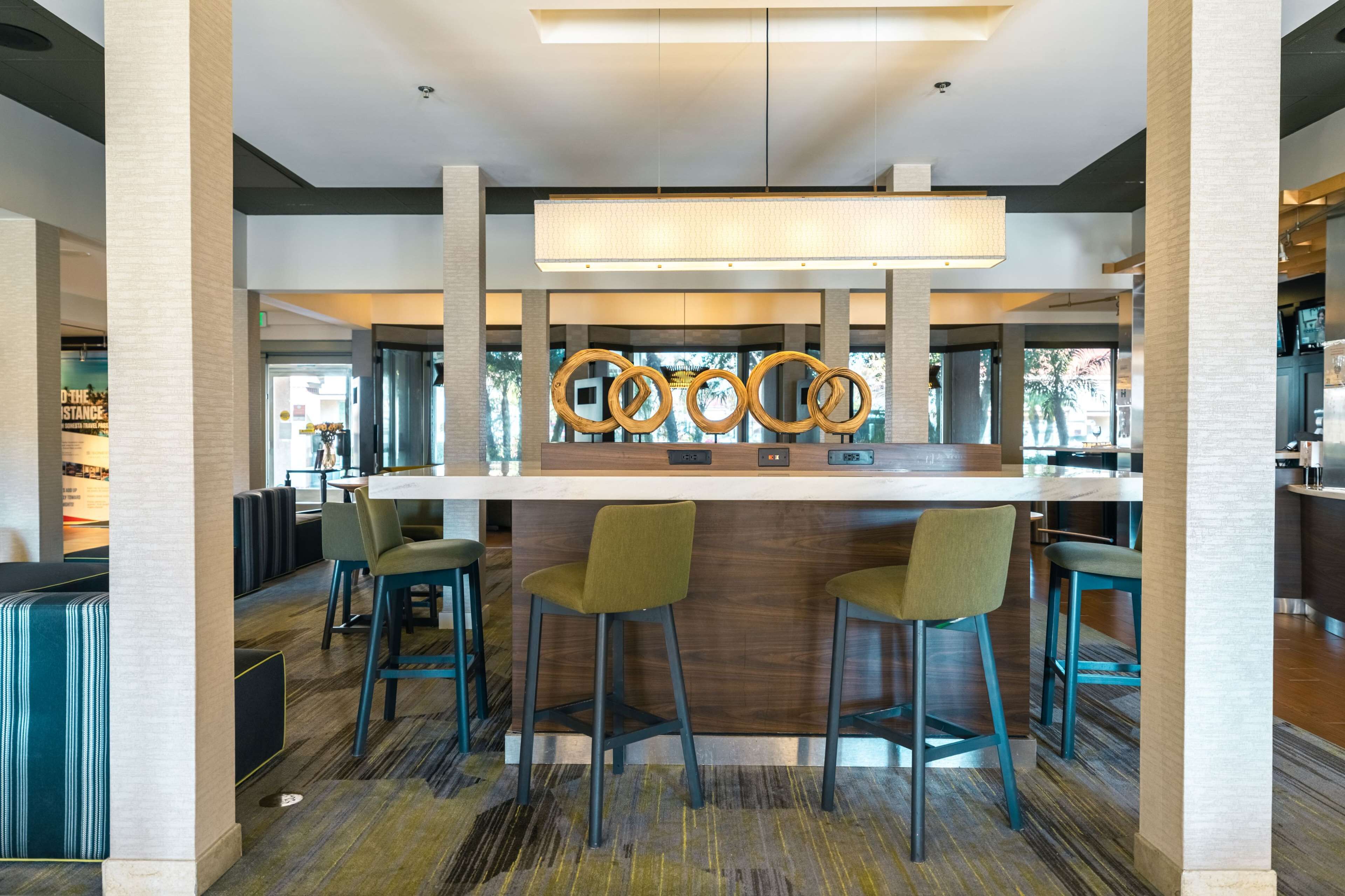Zona de bar moderna con mostrador de madera, taburetes verdes y una pared decorativa con elementos circulares.