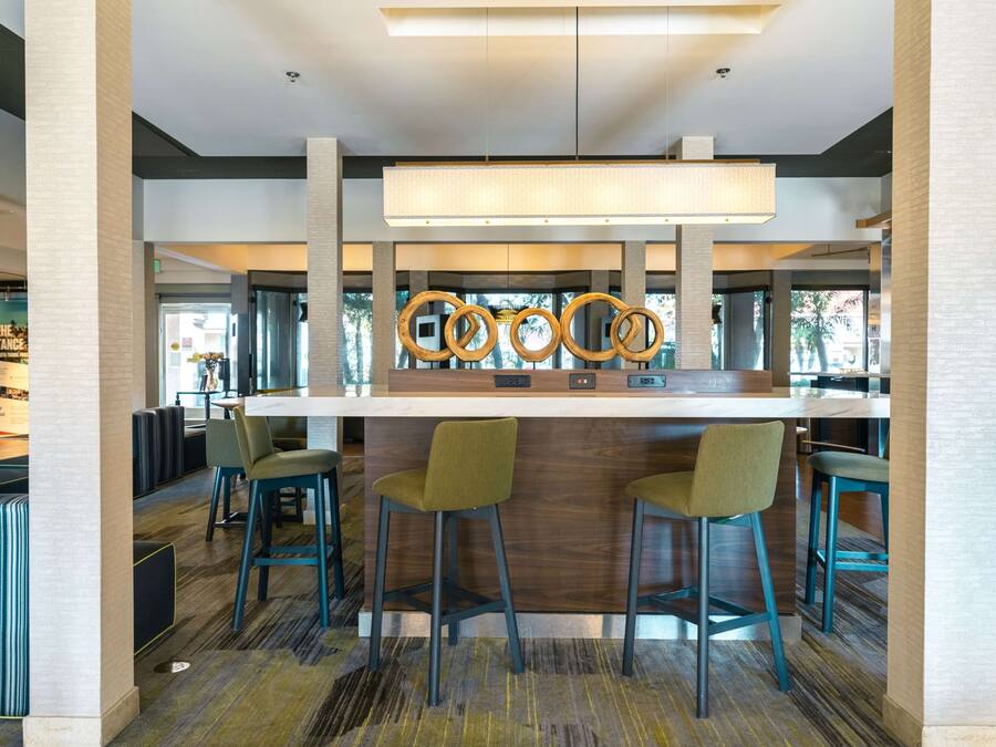 Un espace bar moderne avec un comptoir en bois, des tabourets de bar verts et un mur décoratif agrémenté d’éléments circulaires.