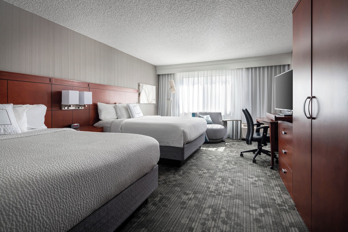 A hotel room with two beds, a desk, a chair, a TV, and a wardrobe.