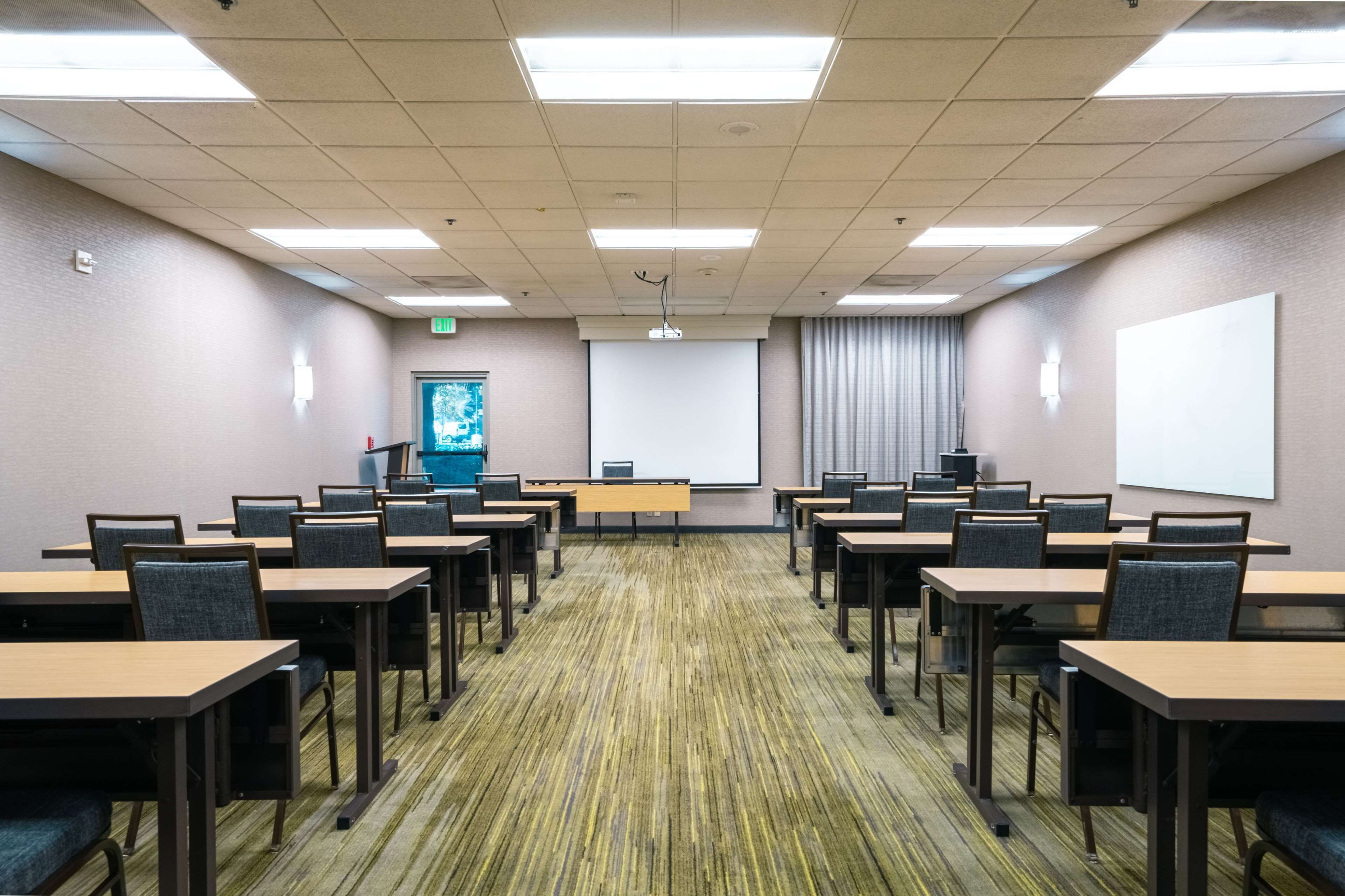 Une salle de conférence équipée de plusieurs tables et chaises, d’un écran de projection et d’un écran de présentation.