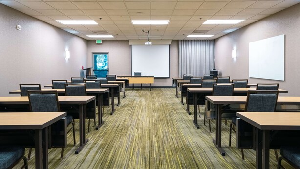A conference room with multiple tables and chairs, a projector screen, and a presentation screen. - Sonesta Select Camarillo (Camarillo)