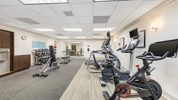 Un gimnasio con máquinas de cardio, equipo de pesas y suelo de madera.
