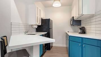 Una cocina compacta con armarios blancos, un refrigerador negro, un microondas y una cafetera.