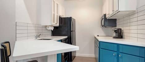 A compact kitchen with white cabinets, a black refrigerator, a microwave, and a coffee maker.