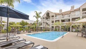 A pool area with lounge chairs and umbrellas, surrounded by a multi-story building with balconies. - Sonesta ES Suites Chatsworth (Chatsworth)