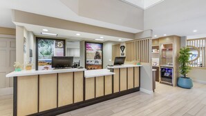 A reception area with a wooden reception desk, a flat-screen TV, a refrigerator, and a potted plant. - Sonesta ES Suites Chatsworth (Chatsworth)