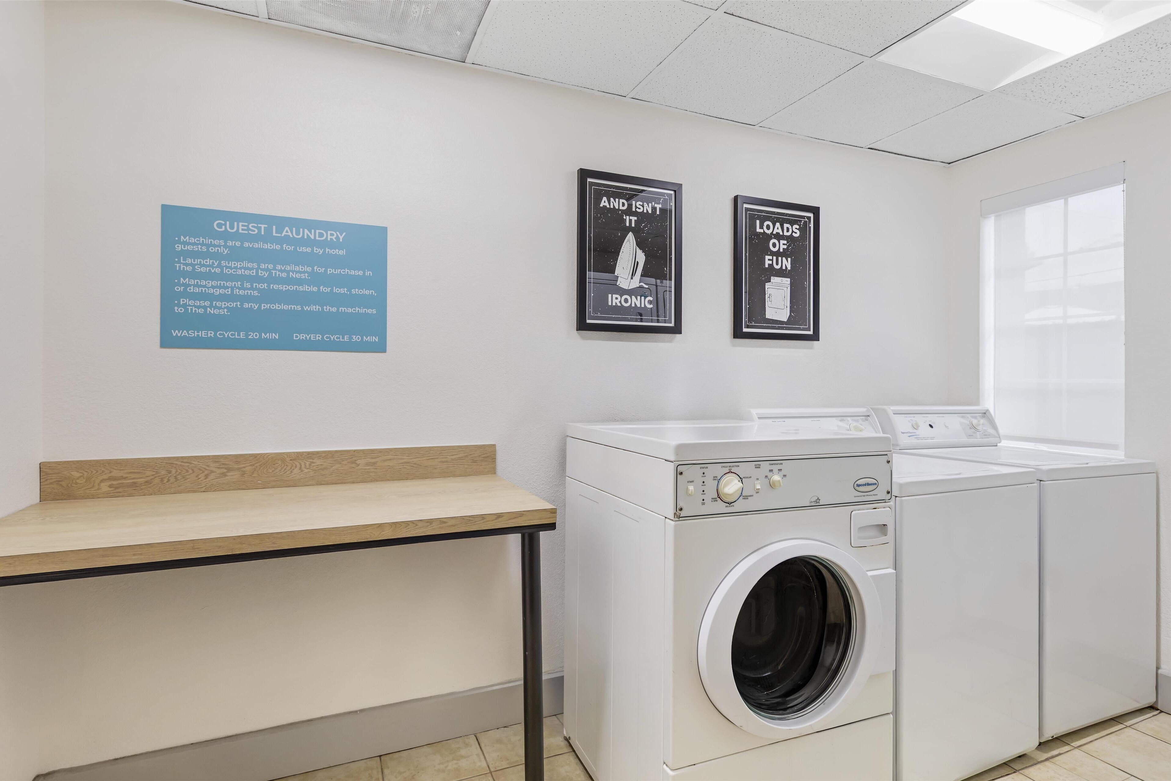 A laundry area with a sign indicating guest laundry availability, a washing machine, and a dryer.