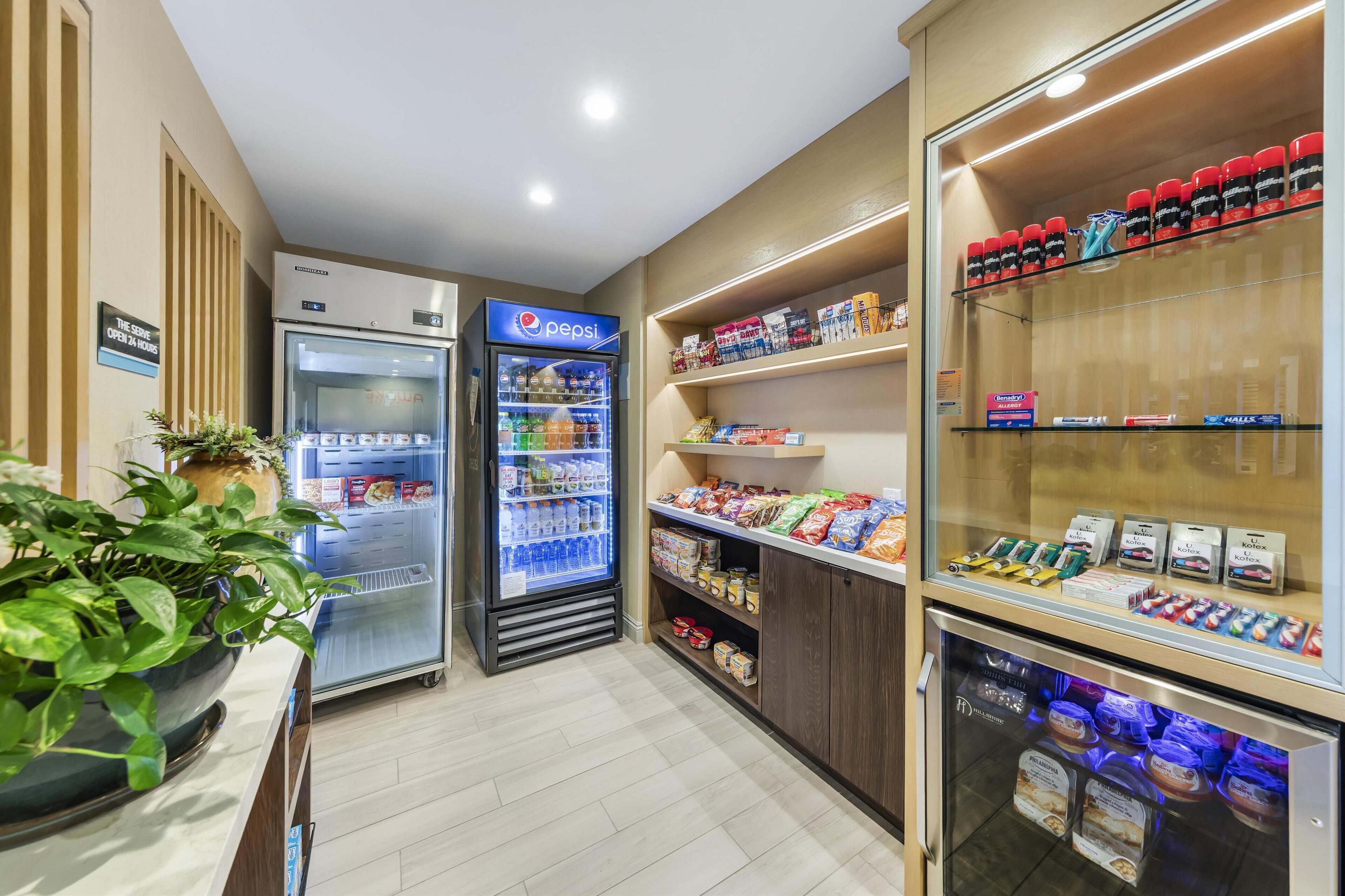 Un vestíbulo de hotel con un refrigerador de Pepsi, estantes con aperitivos y una vitrina refrigerada.