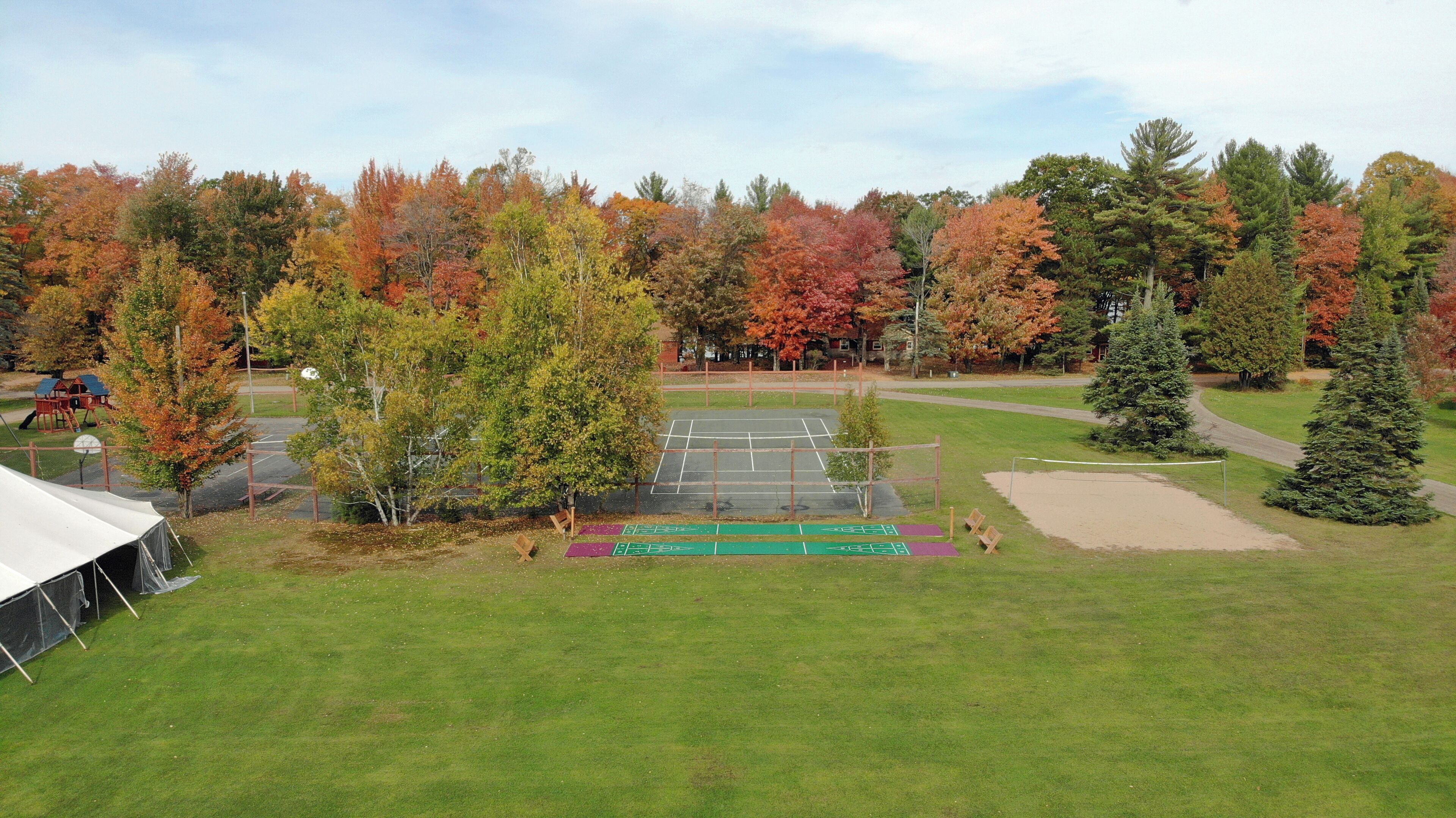 Ein Tennisplatz, umgeben von Bäumen mit Herbstlaub, ein Spielplatz und ein überdachter Bereich.