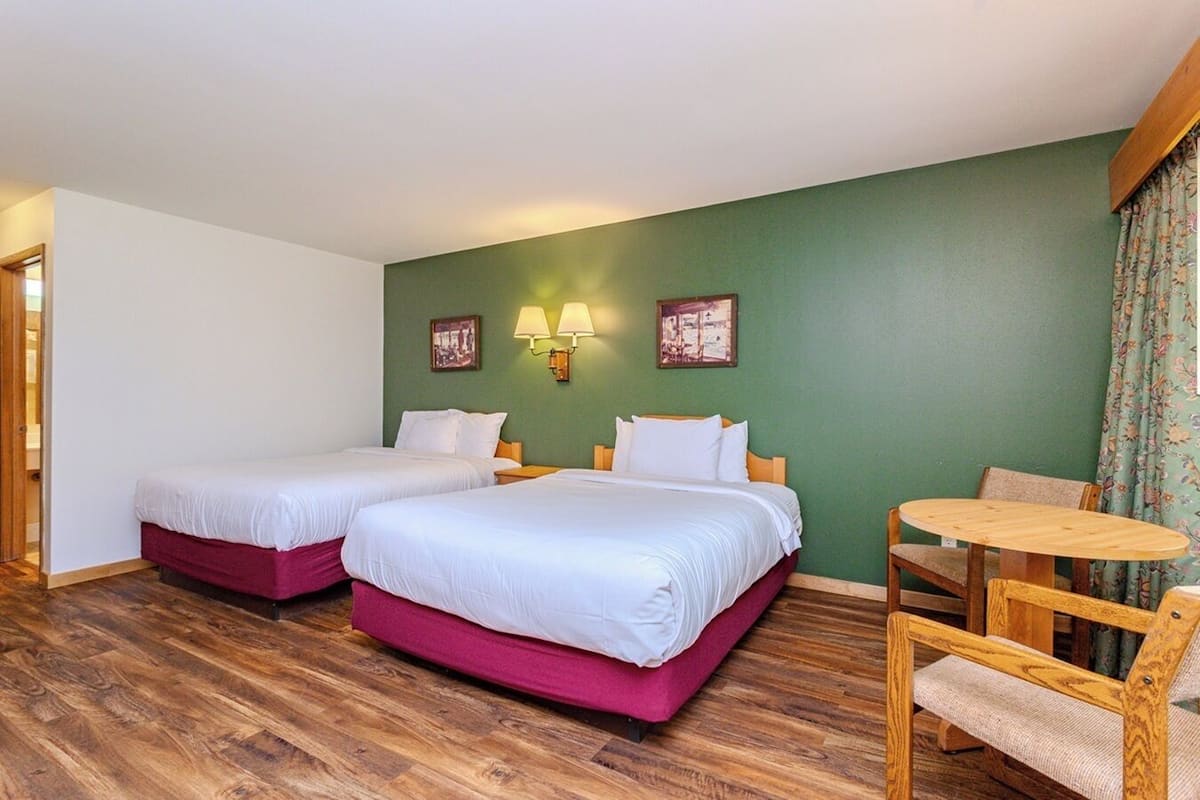 A hotel room with two beds, a small round table, and a chair.