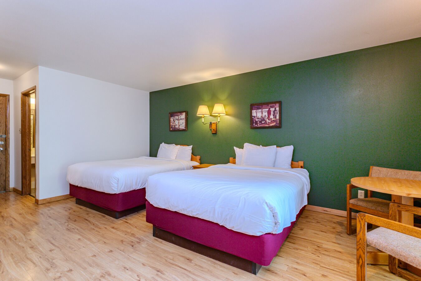 A hotel room with two beds, a wooden table, and two wall-mounted lamps.