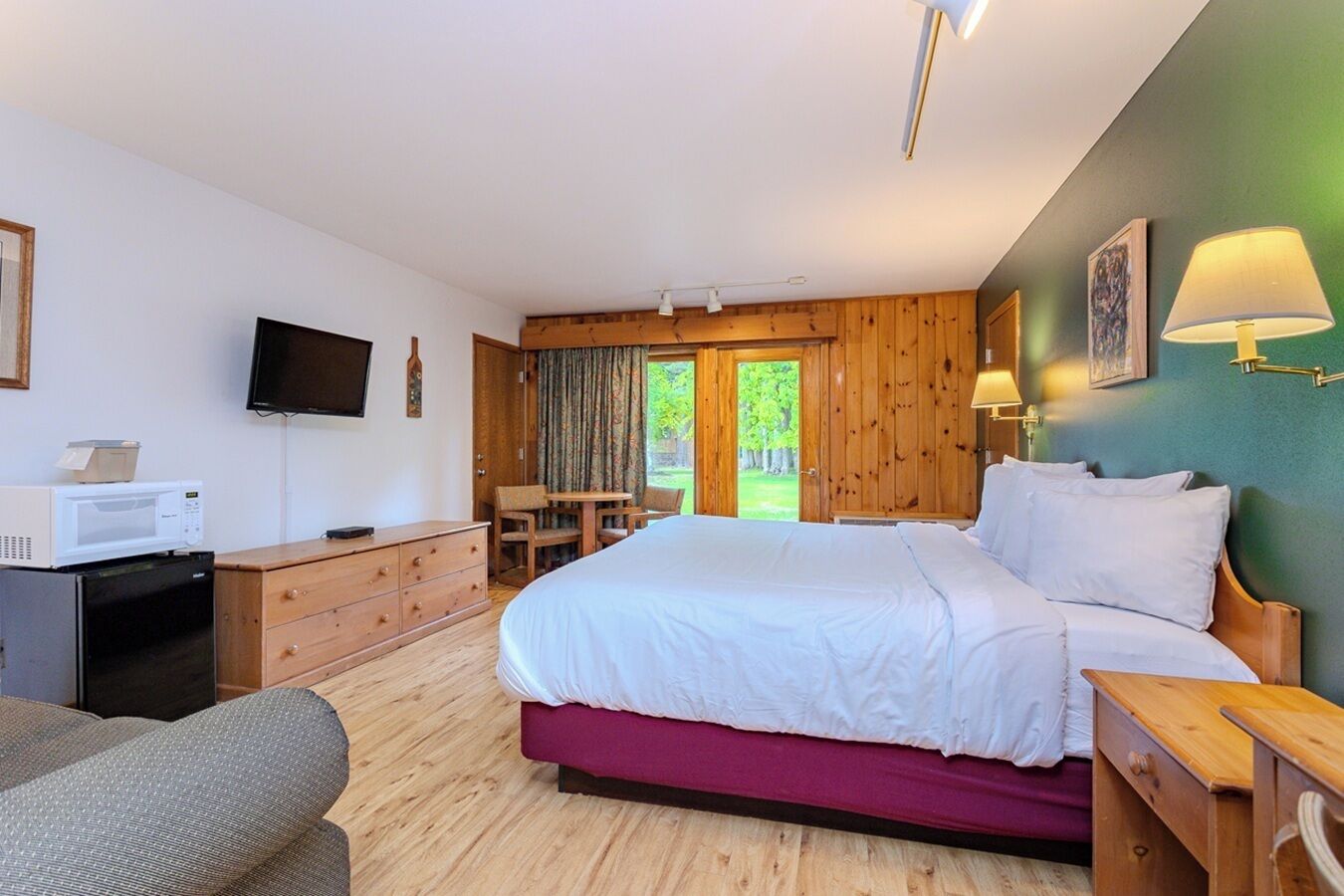 A bedroom with a bed, a desk, a chair, a television, and a microwave.