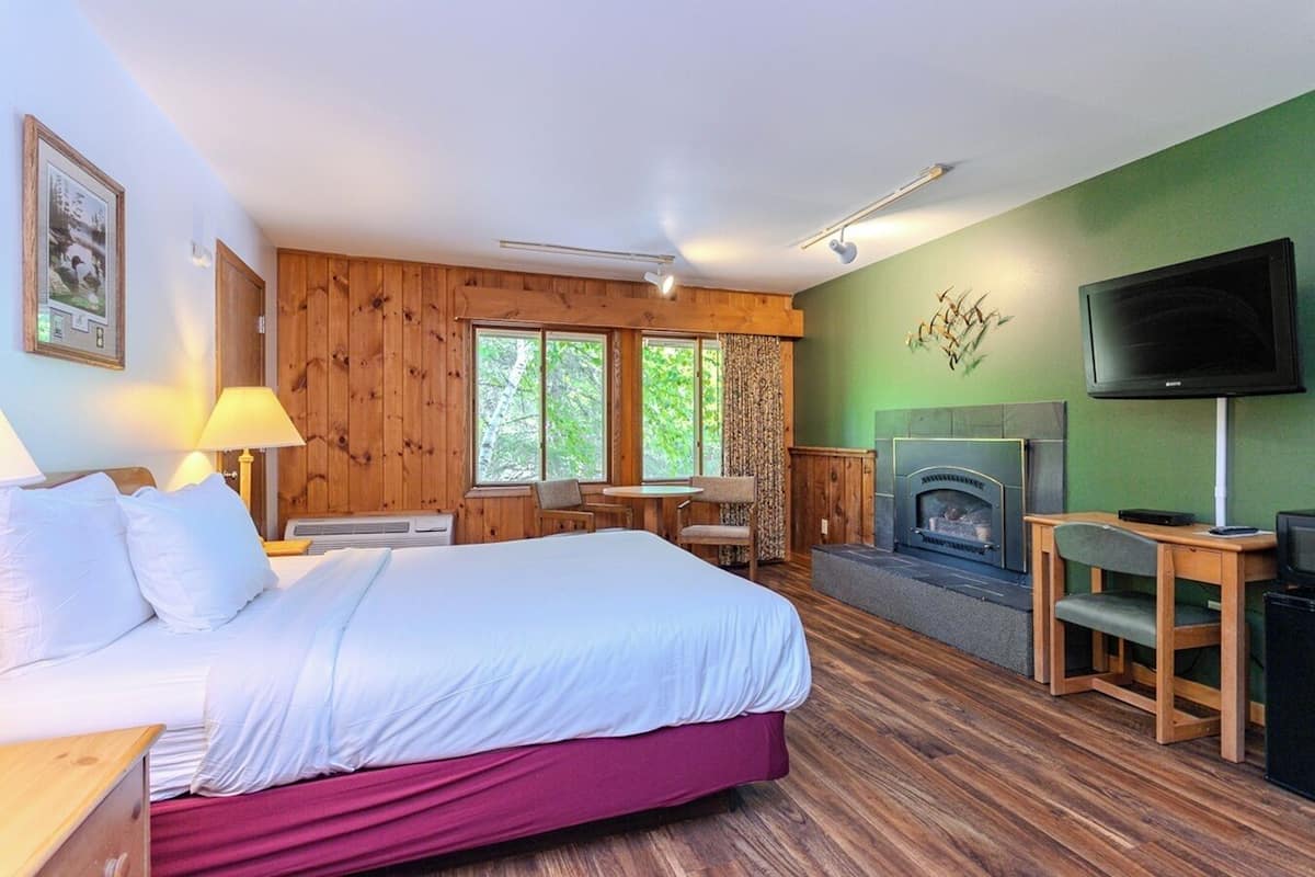 A hotel room with a bed, a television, a fireplace, and a window with curtains.