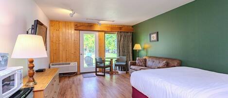 A hotel room with a bed, a desk with a lamp, a chair, a table, and a view of the outdoors.