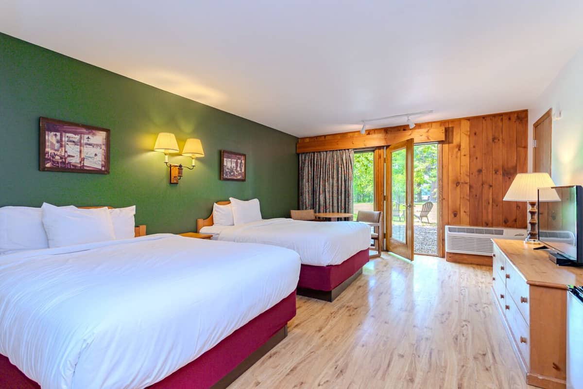A hotel room with two beds, a wooden floor, a television, and a view of the outdoors.