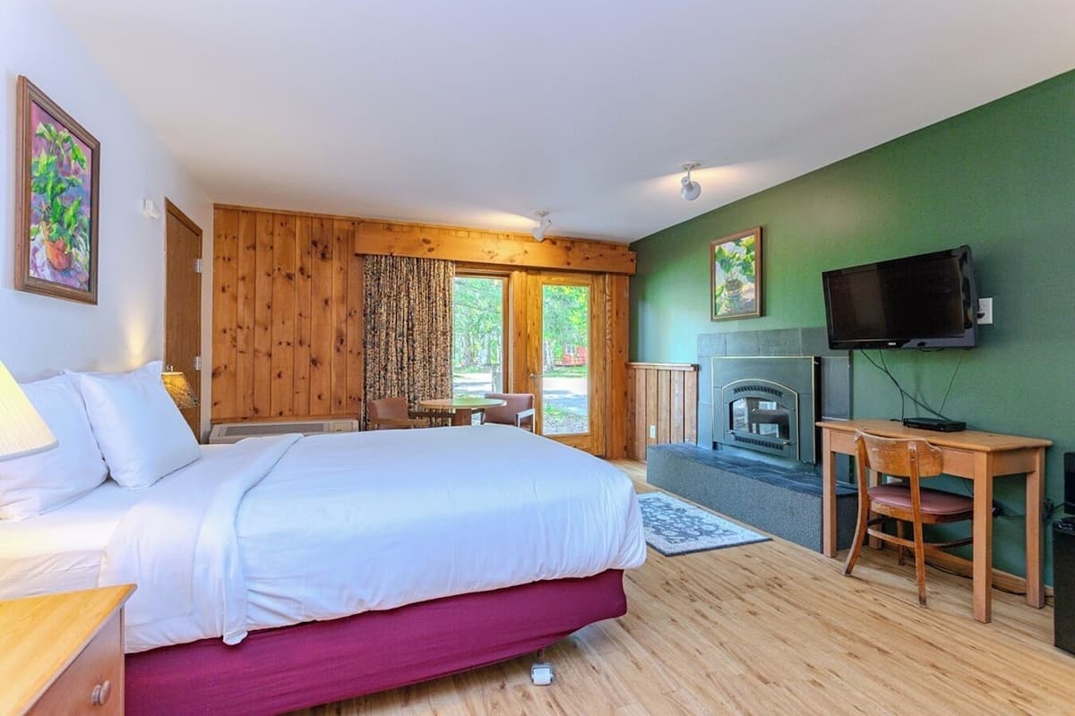 A bedroom with a bed, a desk, a television, and a fireplace.
