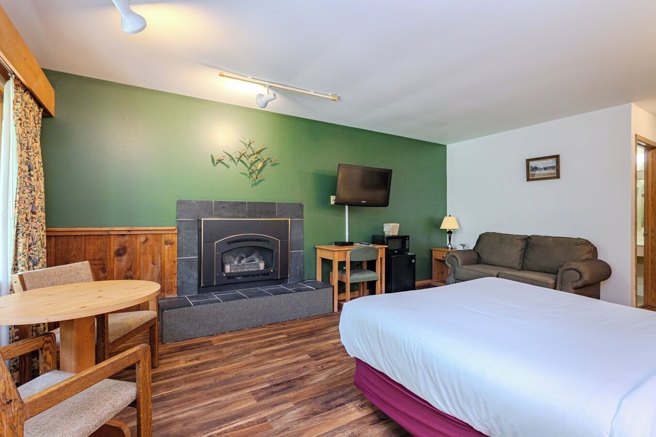 A hotel room with a fireplace, a bed, a sofa, a TV, and a small table with a chair.