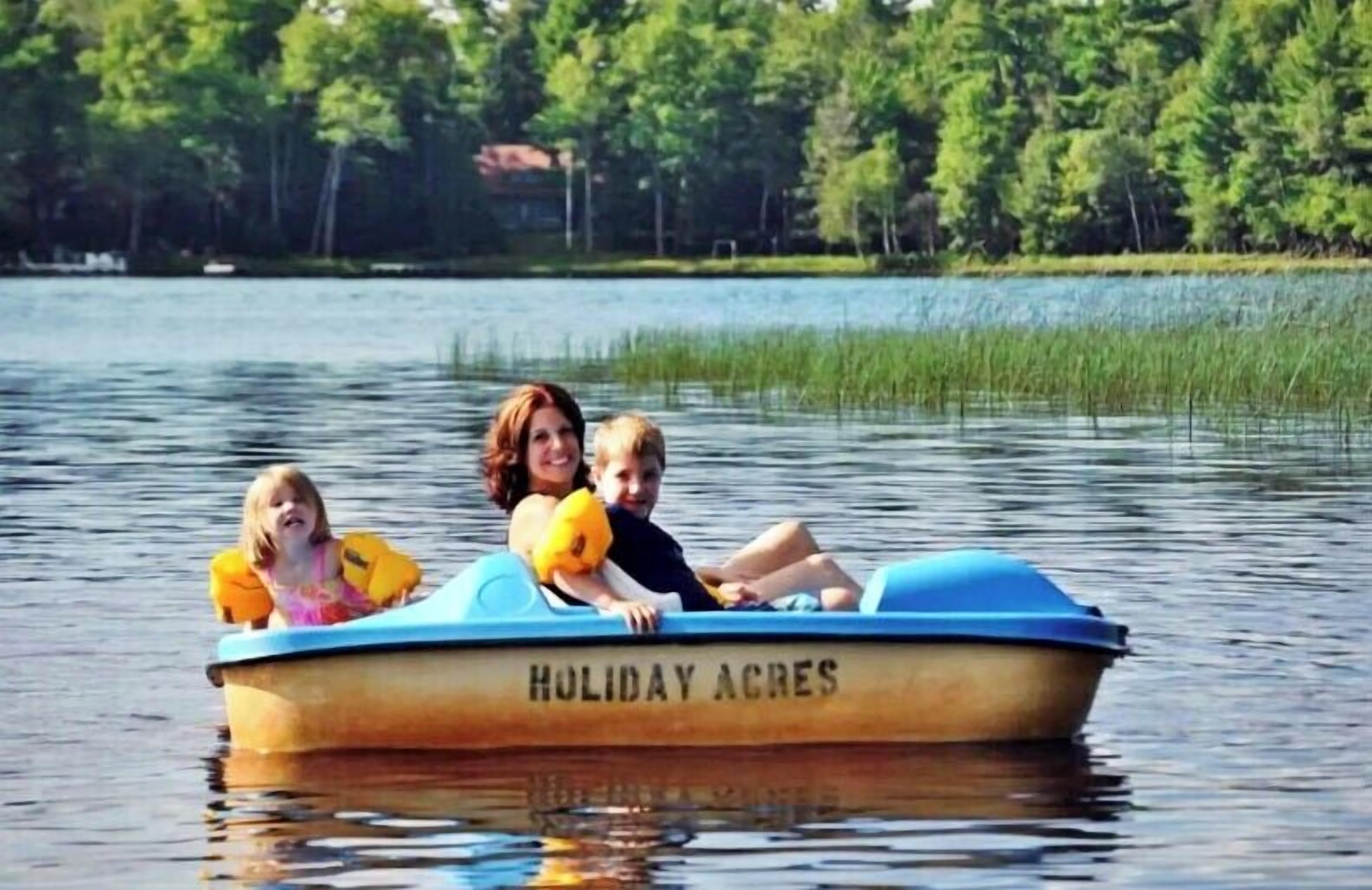 Un barco llamado 'HULIDAY ACRES' en un lago con un bosque al fondo.