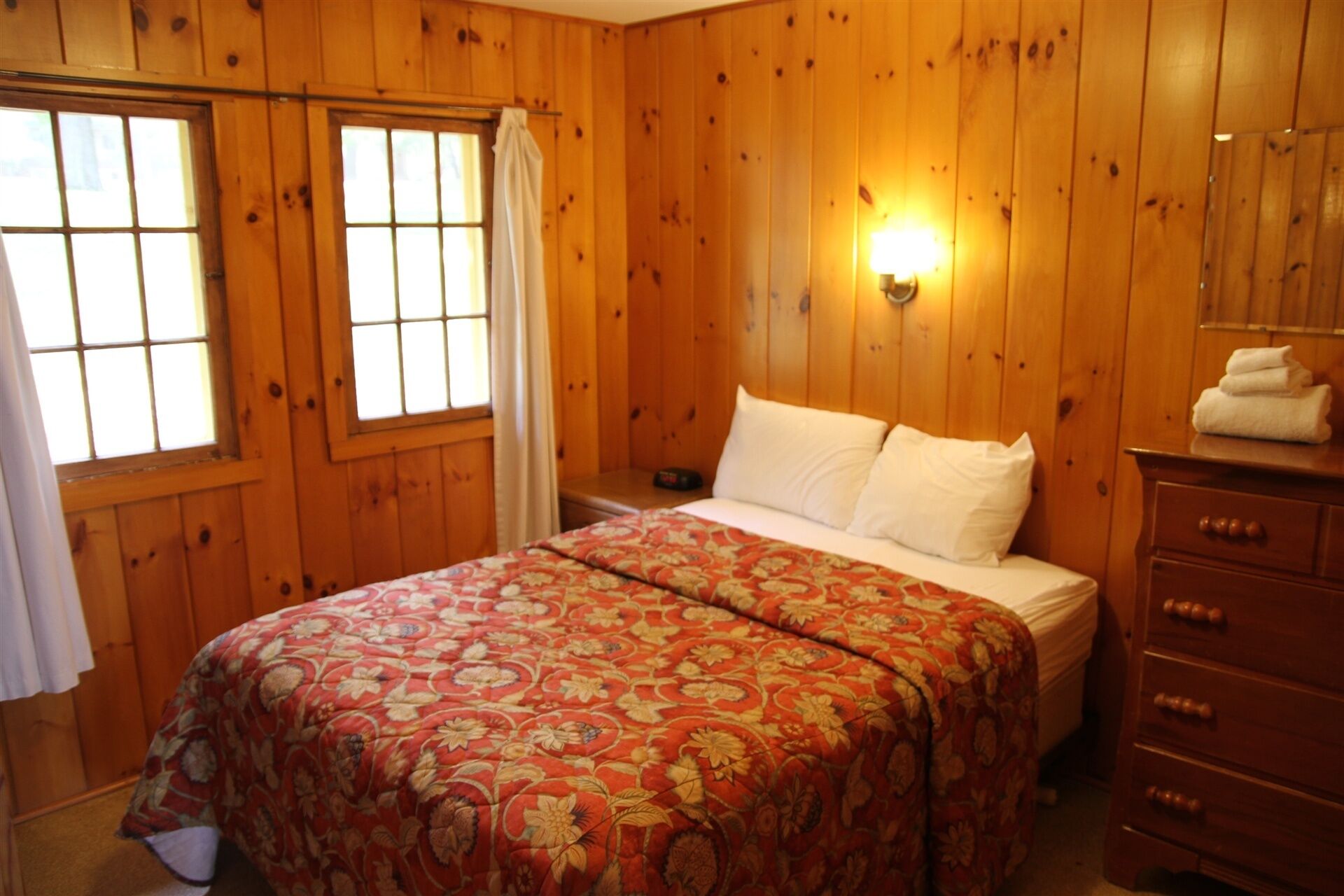 A wooden-paneled room with a bed, a dresser, and a nightstand.