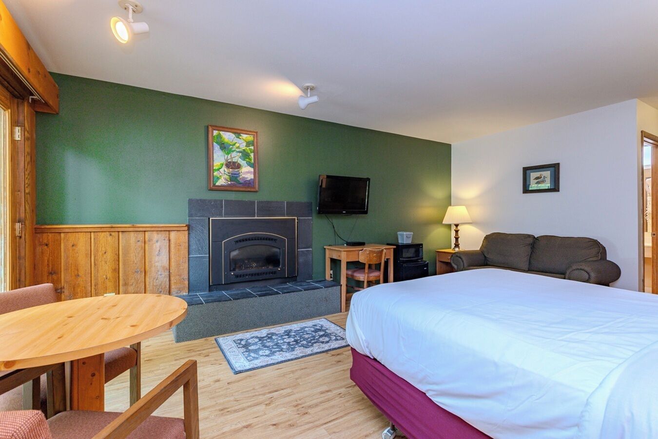 A hotel room with a bed, a small table, a chair, a fireplace, a TV, and a lamp.